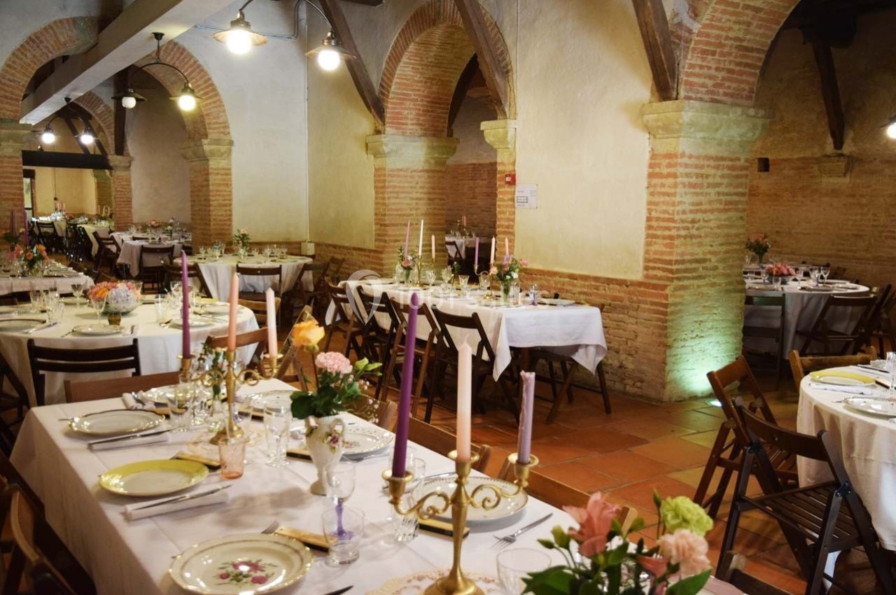 Salle voûtée avec tables dressées pour un repas, décorée de chandeliers, fleurs et vaisselle élégante.