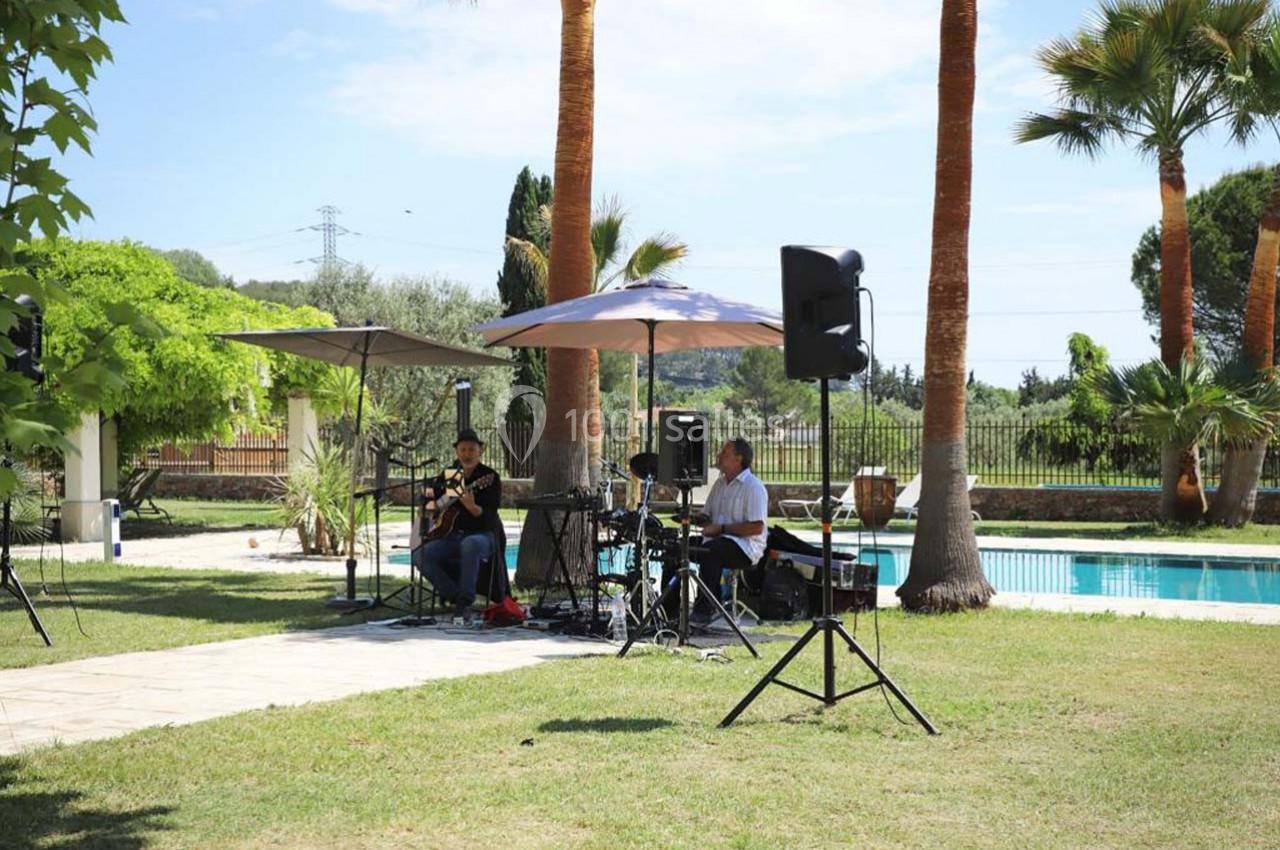 Deux musiciens jouent en plein air près d'une piscine, entourés de palmiers et d'équipements sonores.