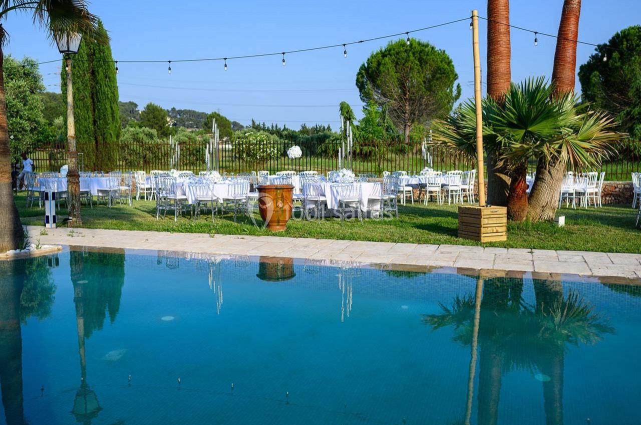 Tables dressées en extérieur près d'une piscine, entourées de palmiers et de verdure sous un ciel dégagé.