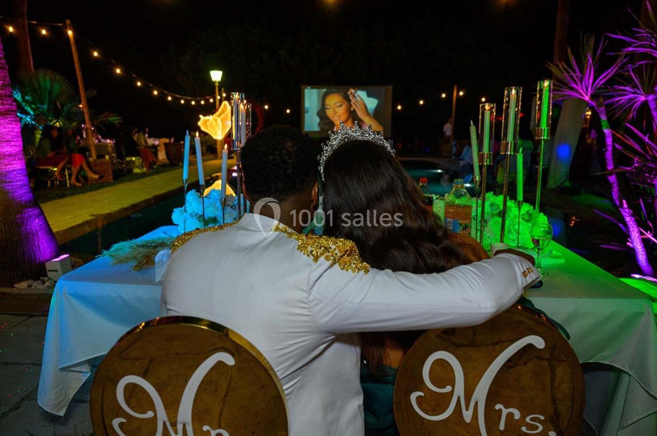 Un couple assis de dos, vêtu élégamment, regarde une projection en extérieur sous des lumières décoratives.