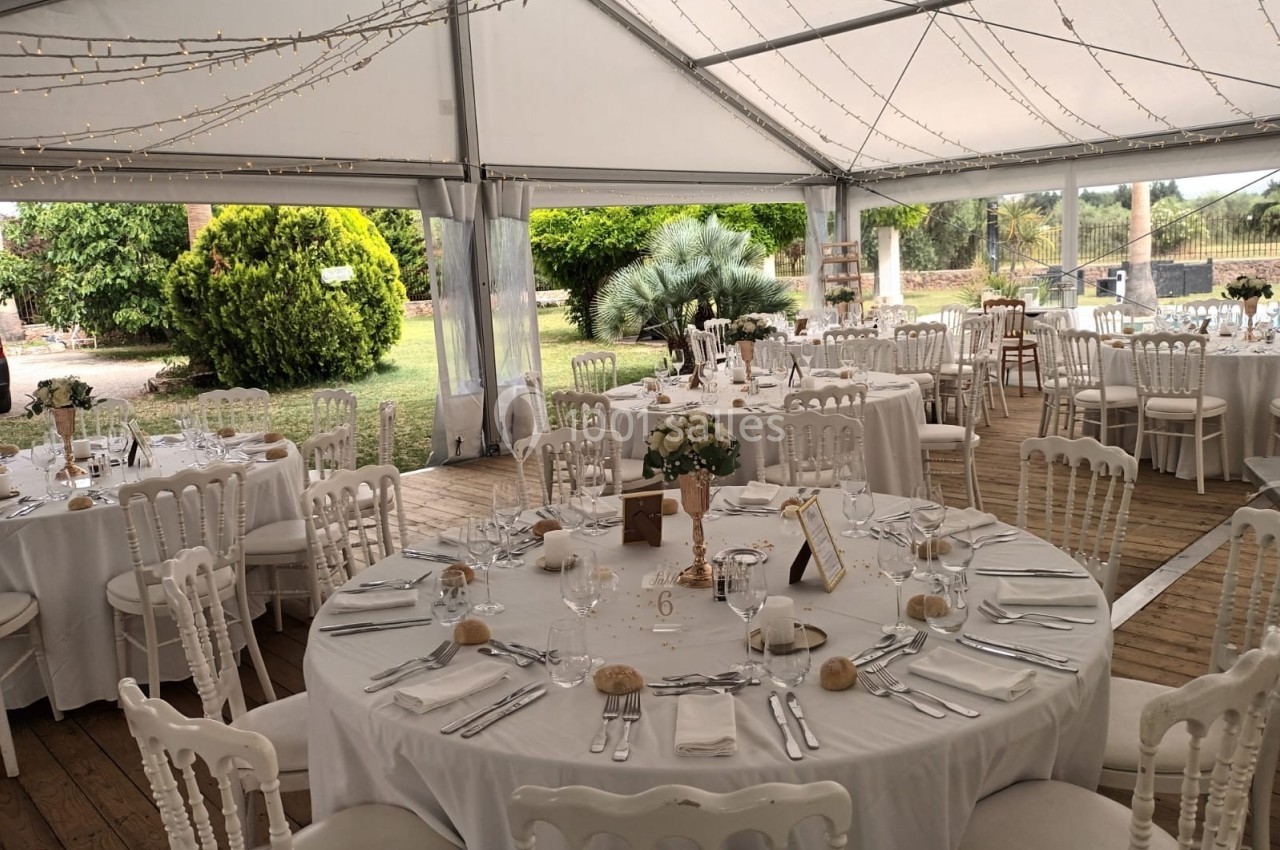 Salle de réception sous une tente avec tables rondes dressées, nappes blanches et décorations élégantes.