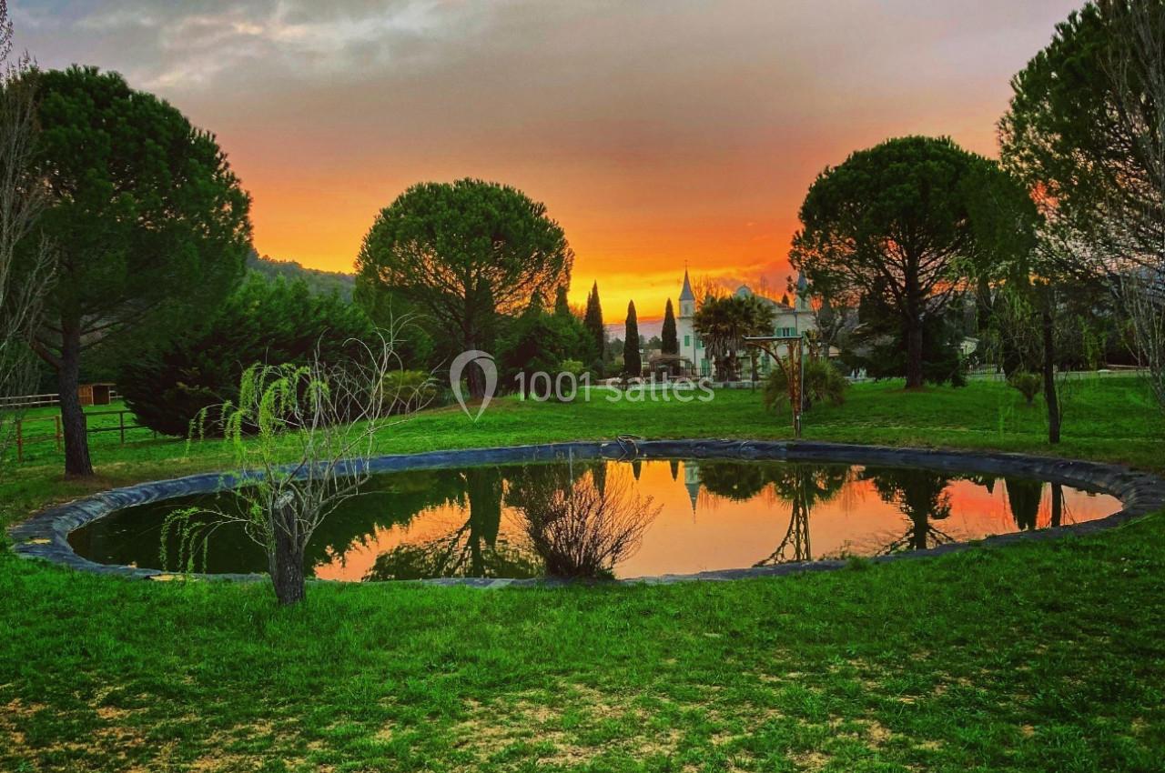 Étang entouré de verdure avec un coucher de soleil coloré et des arbres reflétés dans l'eau.