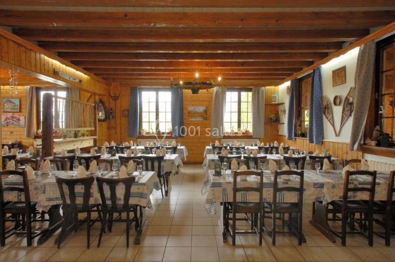 Salle de restaurant rustique avec tables dressées, poutres apparentes et décoration montagnarde.