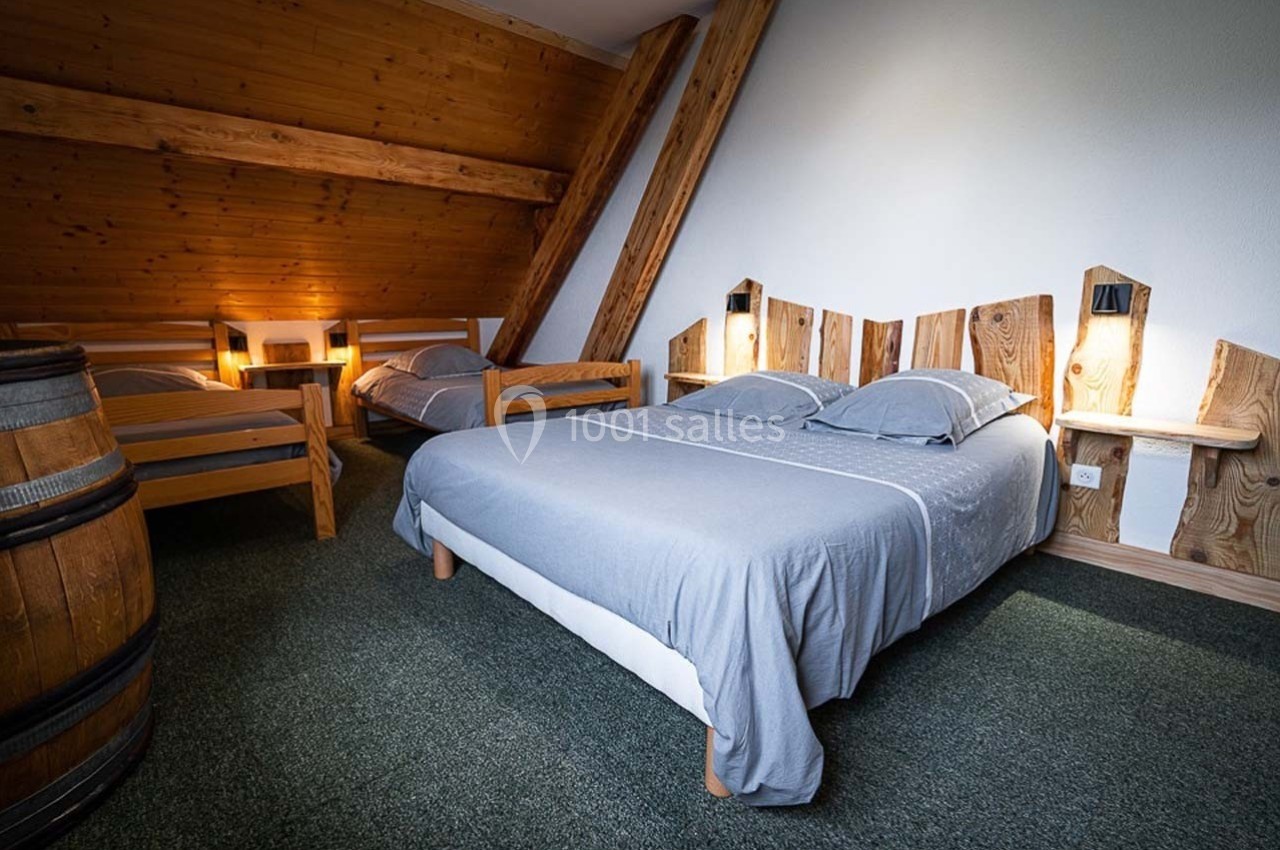 Chambre mansardée avec lit double, deux lits simples, mobilier en bois et éclairage chaleureux.