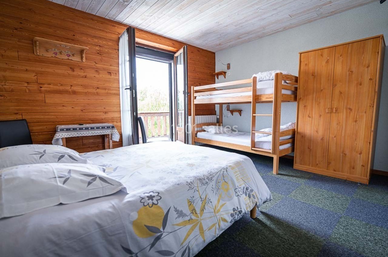 Chambre avec lit double, lits superposés, armoire en bois et balcon, décorée avec des murs en bois et un plafond clair.
