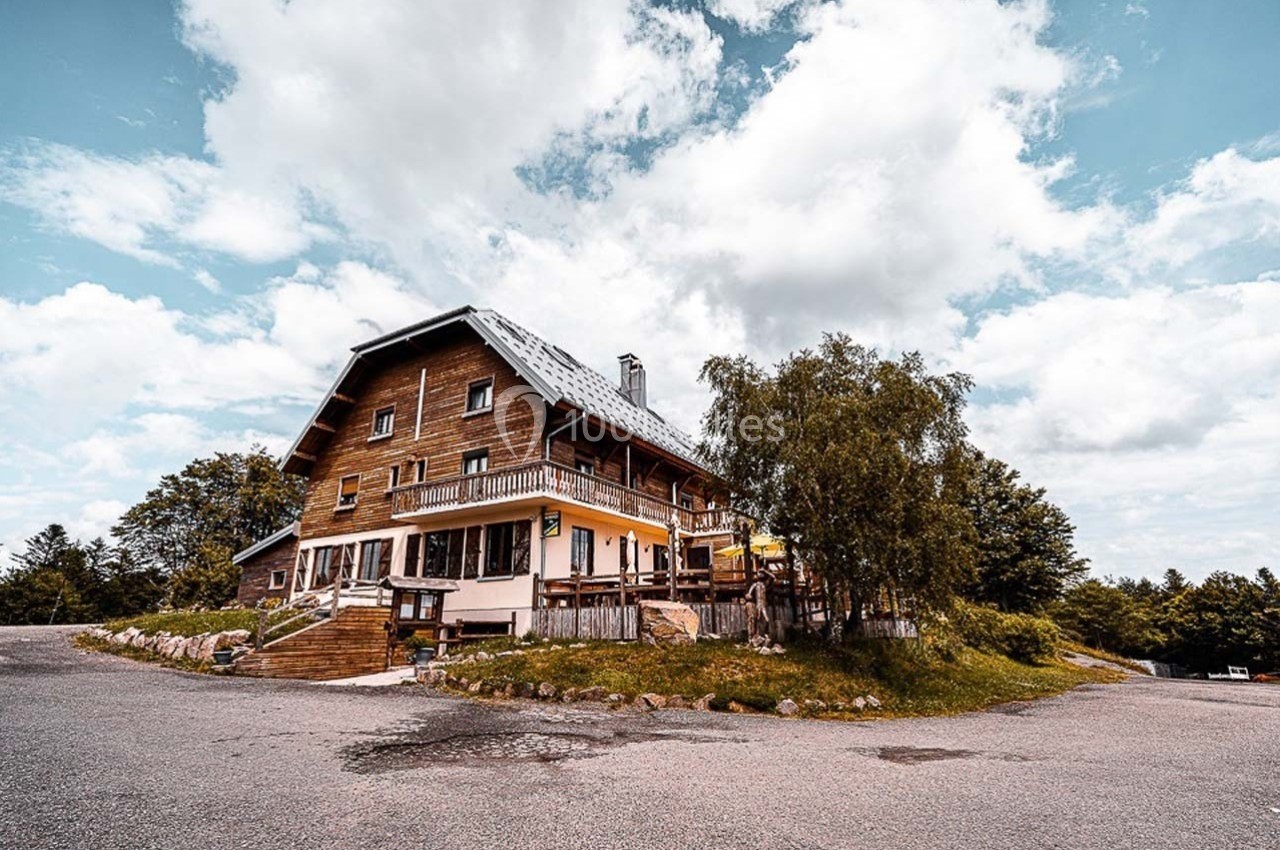 Chalet en bois sur une route dégagée, entouré d'arbres et sous un ciel partiellement nuageux.