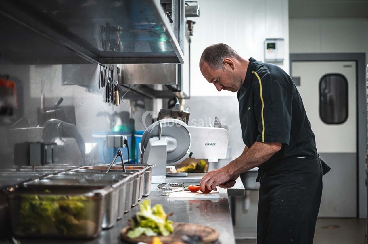 Un cuisinier prépare des légumes sur un plan de travail dans une cuisine professionnelle.