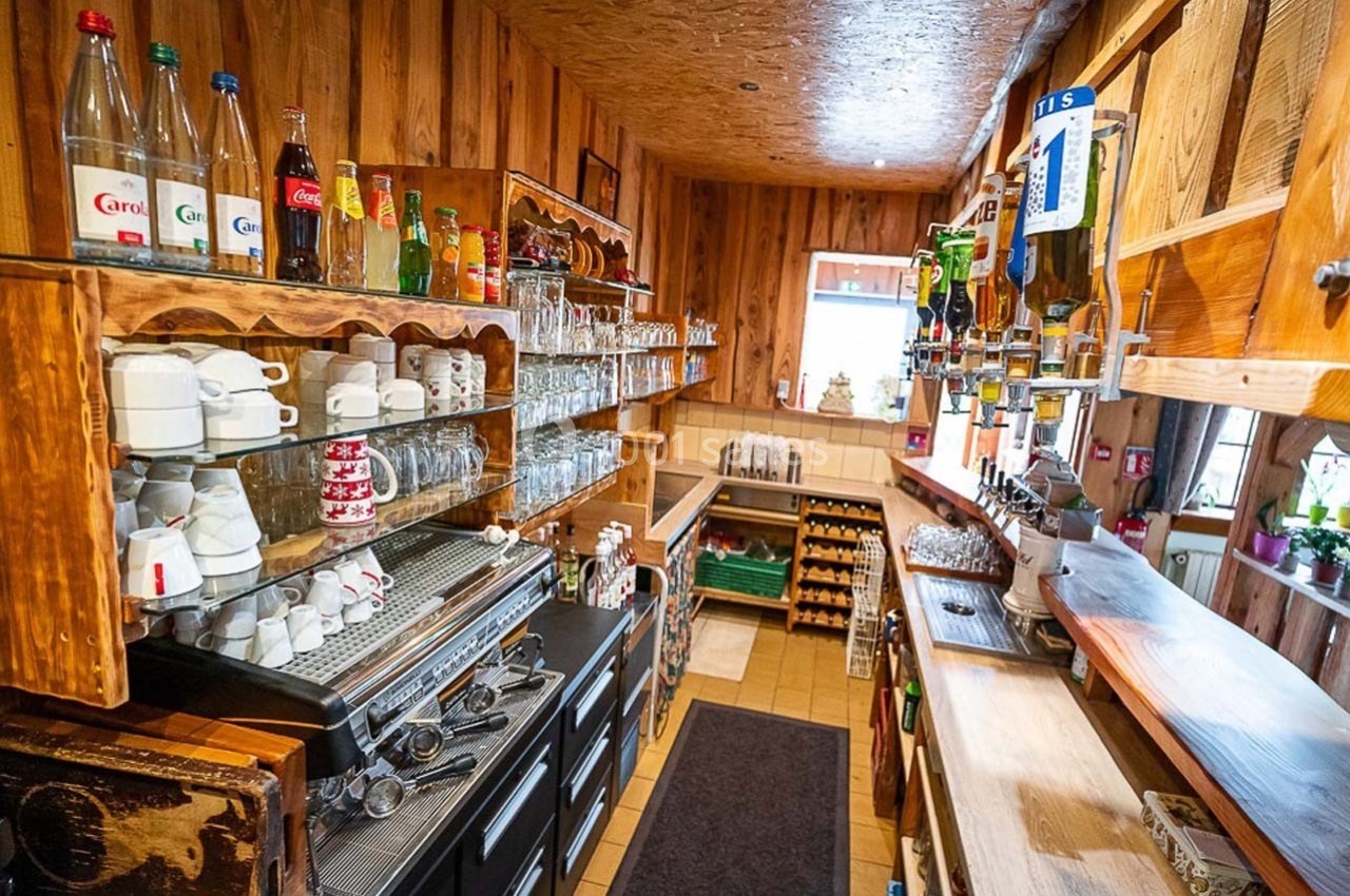 Intérieur d'un bar en bois avec étagères remplies de verres, tasses et bouteilles, et un comptoir équipé.