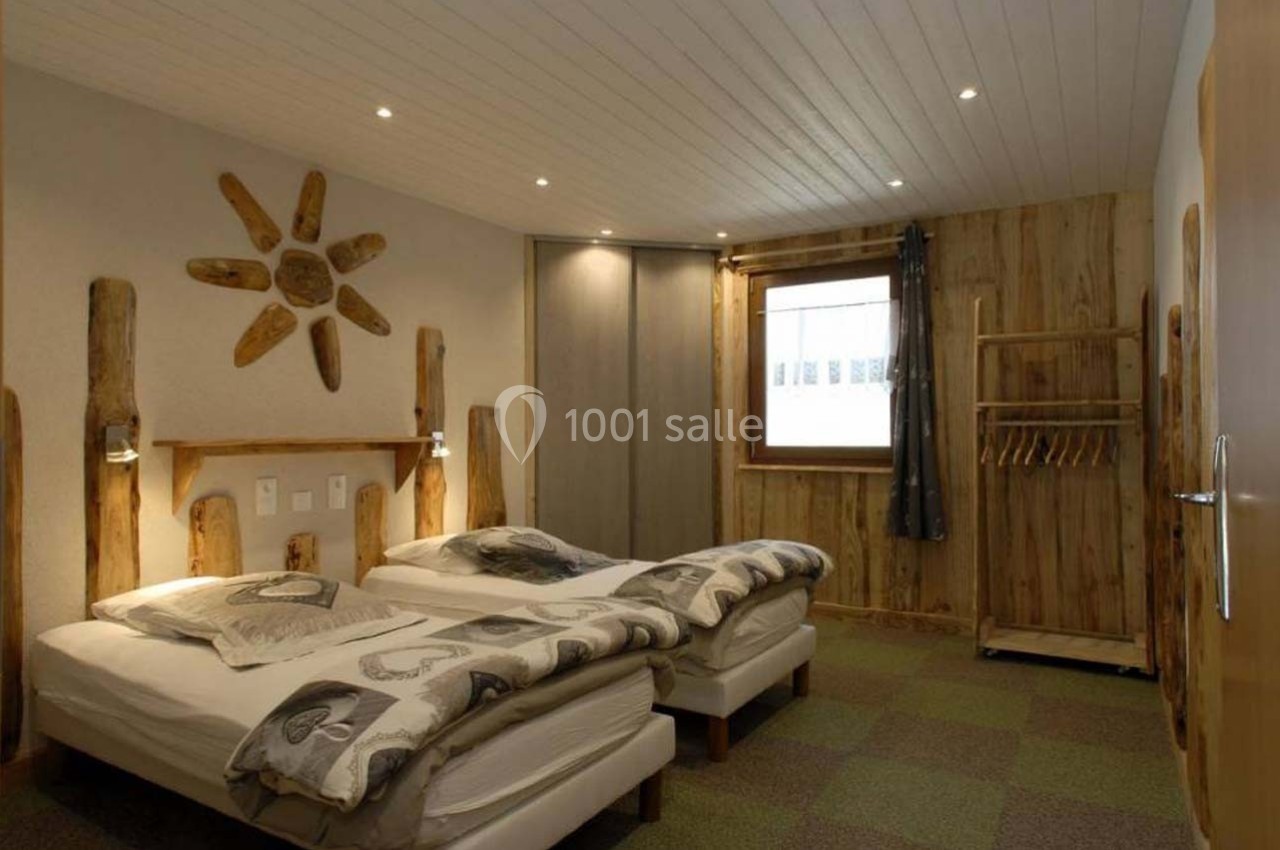 Chambre avec deux lits simples, décor en bois naturel, éclairage doux et fenêtre avec rideau sombre.