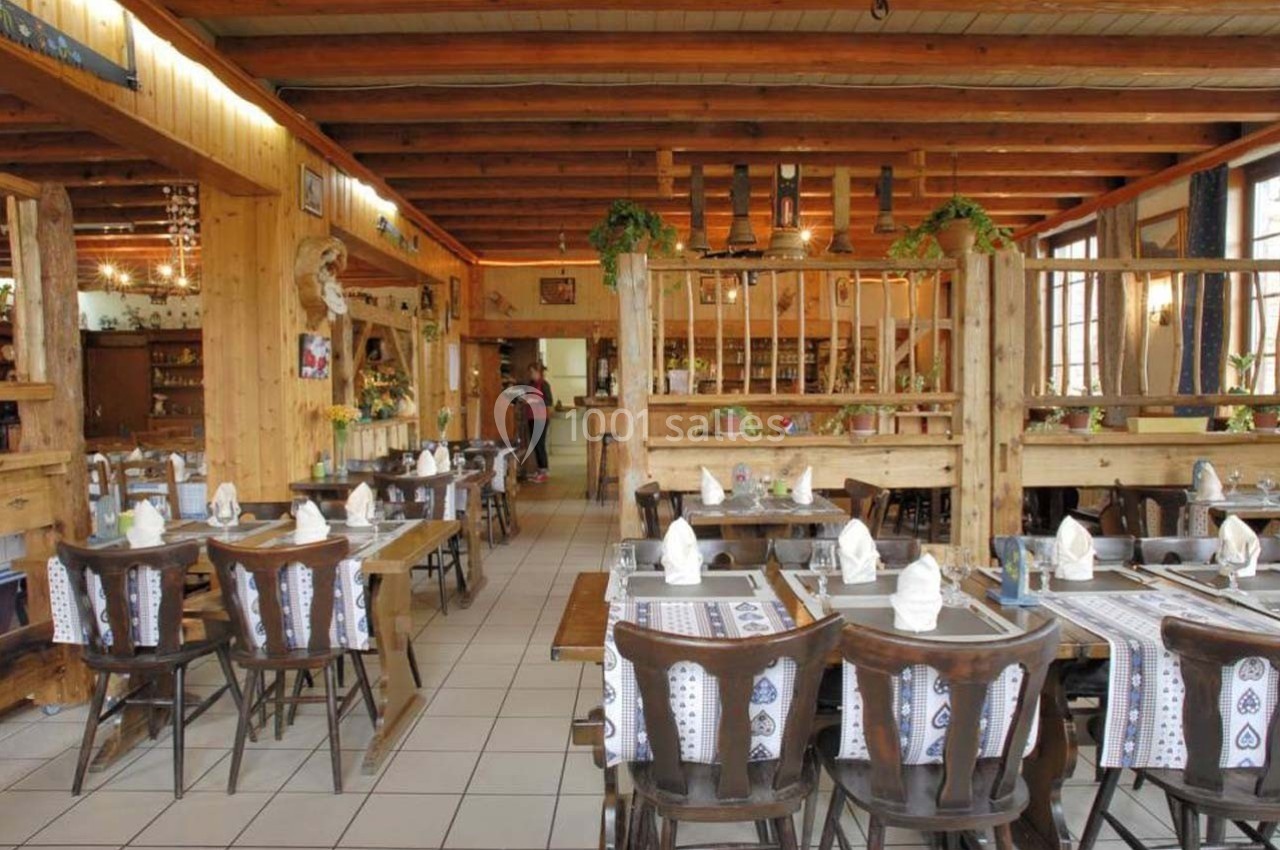 Salle de restaurant rustique avec tables en bois dressées, nappes à motifs et décoration chaleureuse en bois.
