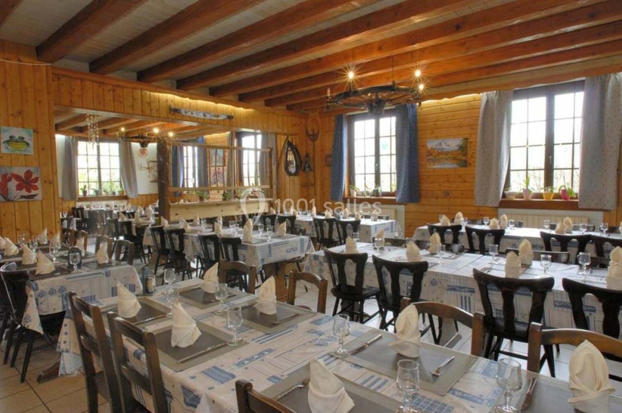Salle de restaurant lumineuse avec tables dressées, nappes à motifs bleus et poutres apparentes au plafond.