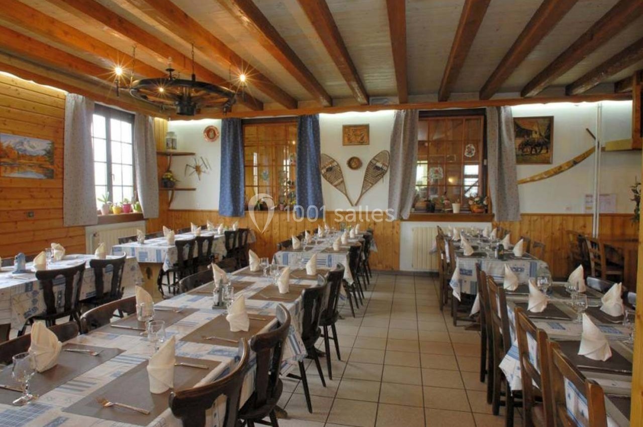 Salle de restaurant rustique avec tables dressées, nappes bleues et blanches, et décoration en bois aux murs.