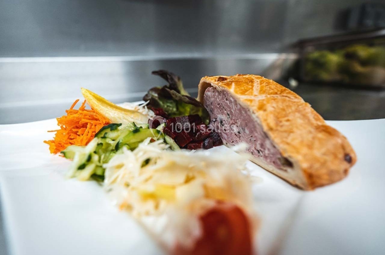 Part de pâté en croûte servie avec des légumes frais râpés et une salade colorée sur une assiette blanche.