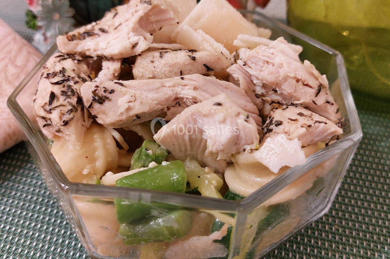 Salade composée avec pâtes, morceaux de poulet assaisonné, haricots verts et légumes dans un bol en verre.