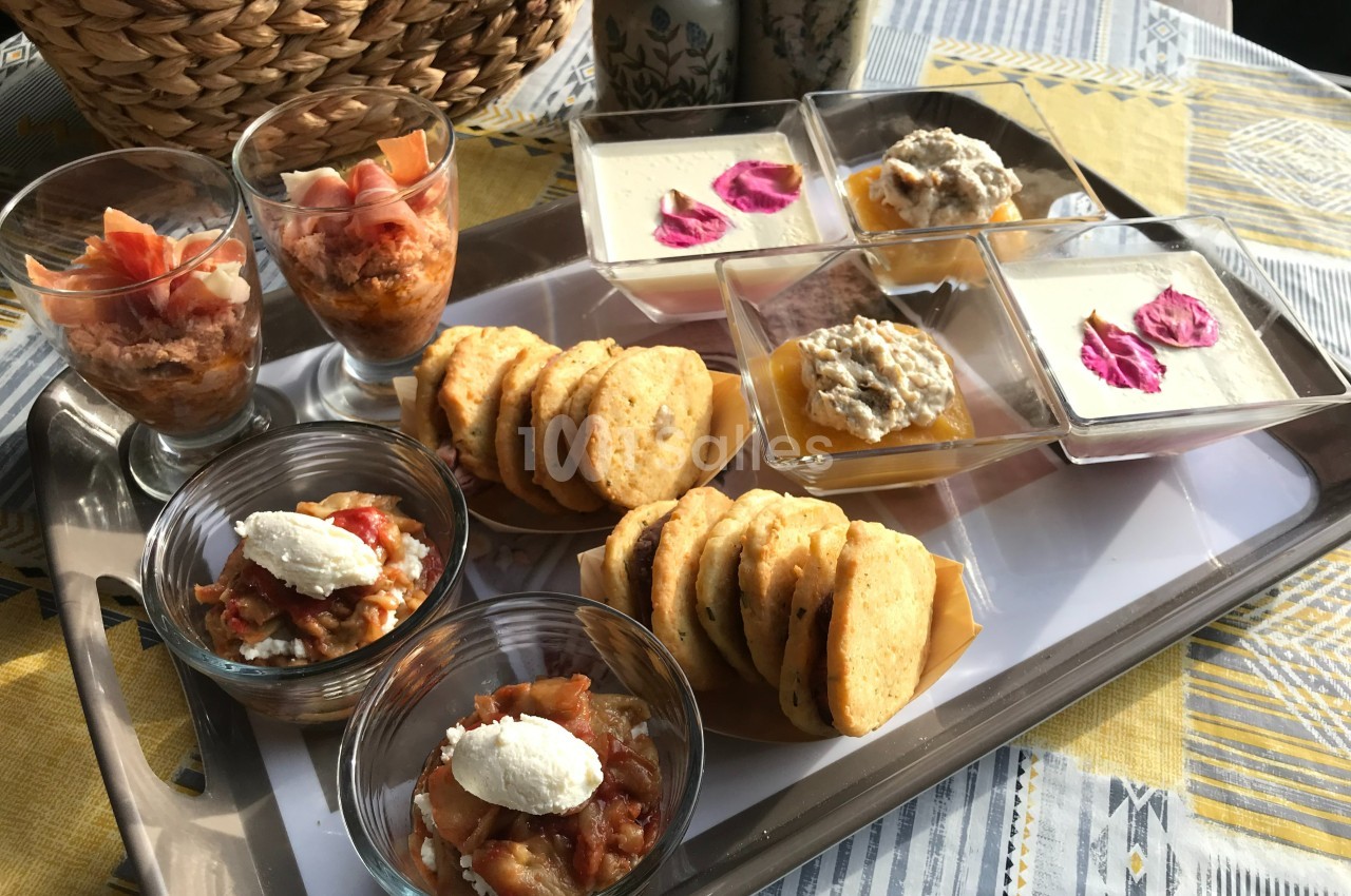 Plateau de verrines salées, biscuits apéritifs et desserts présentés sur une table avec une nappe colorée.