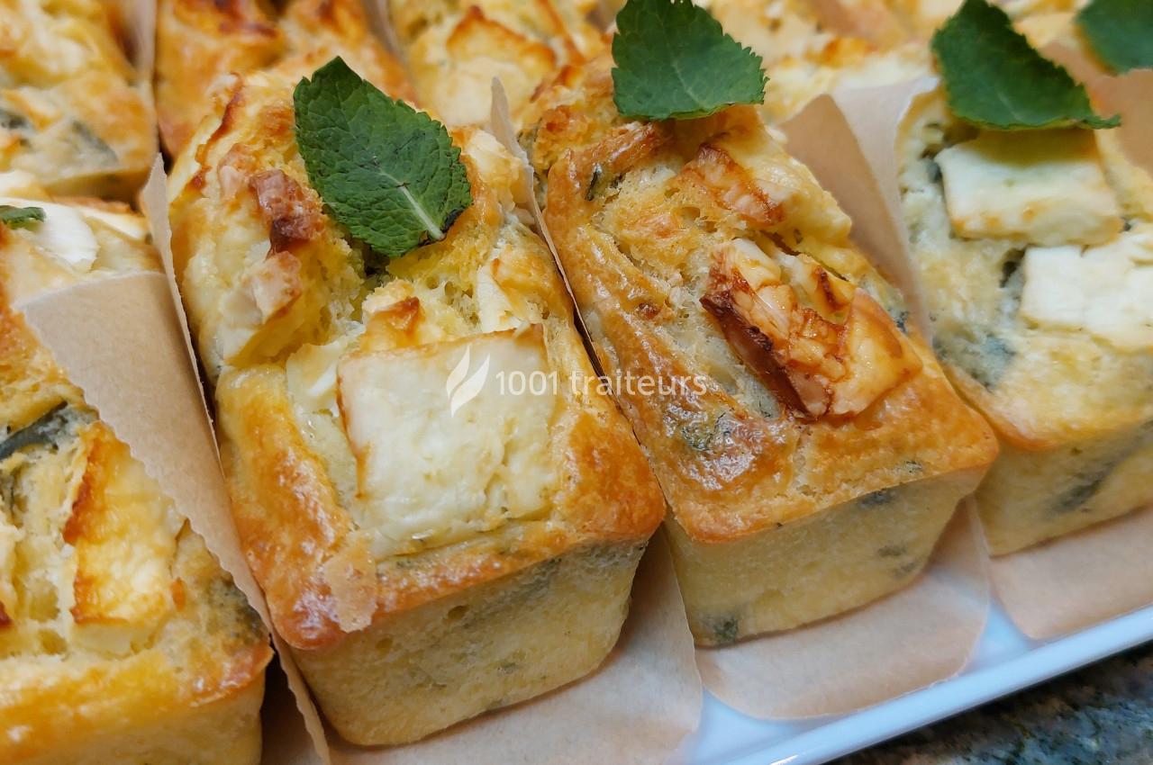 Mini-cakes salés garnis de fromage et décorés de feuilles de menthe, présentés sur un plateau.