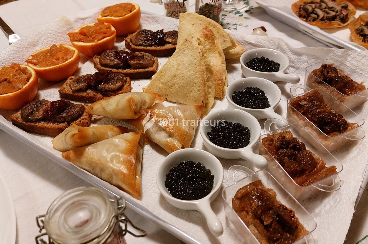 Plateau d'amuse-bouches variés comprenant toasts, samoussas, caviar, figues et oranges garnies, disposé sur une table.