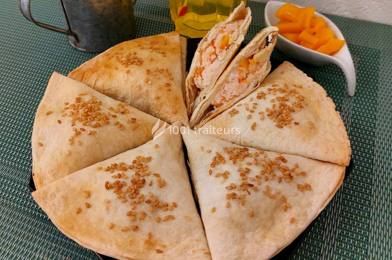 Assiette de tortillas garnies, coupées en parts, avec graines de sésame, accompagnées de morceaux de mangue.