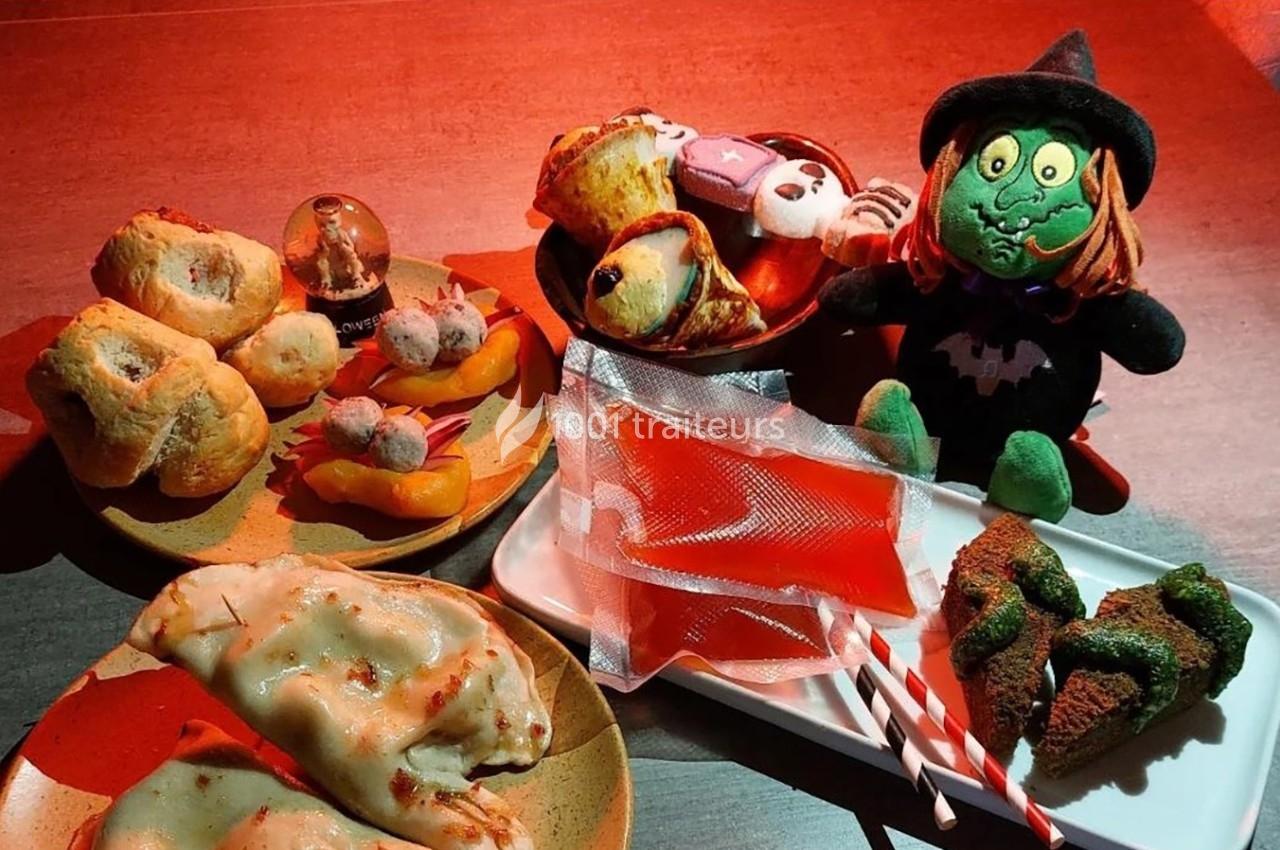 Assortiment de pâtisseries et friandises sur le thème d'Halloween avec une peluche de sorcière en décoration.