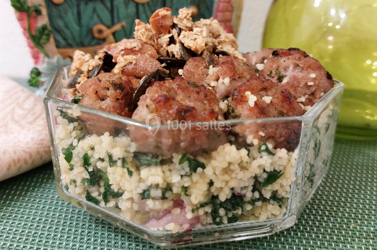 Bol en verre contenant du couscous aux herbes, des boulettes de viande grillées et une garniture croustillante.