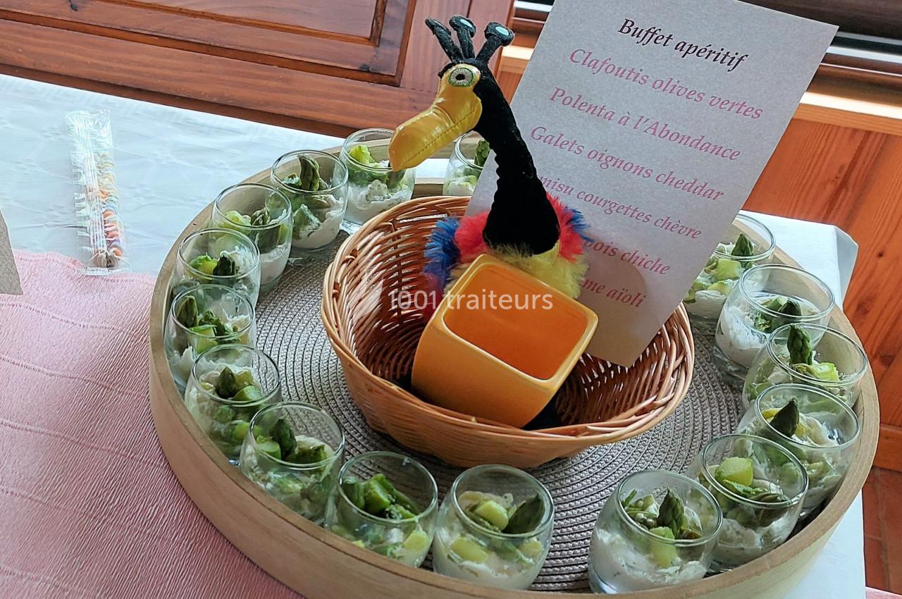 Buffet apéritif avec verrines de légumes verts disposées autour d'une corbeille contenant une décoration colorée.