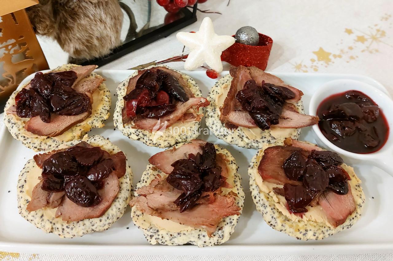 Tranches de viande sur des toasts garnis de graines de pavot et de compote de fruits rouges, présentés sur un plateau blanc.
