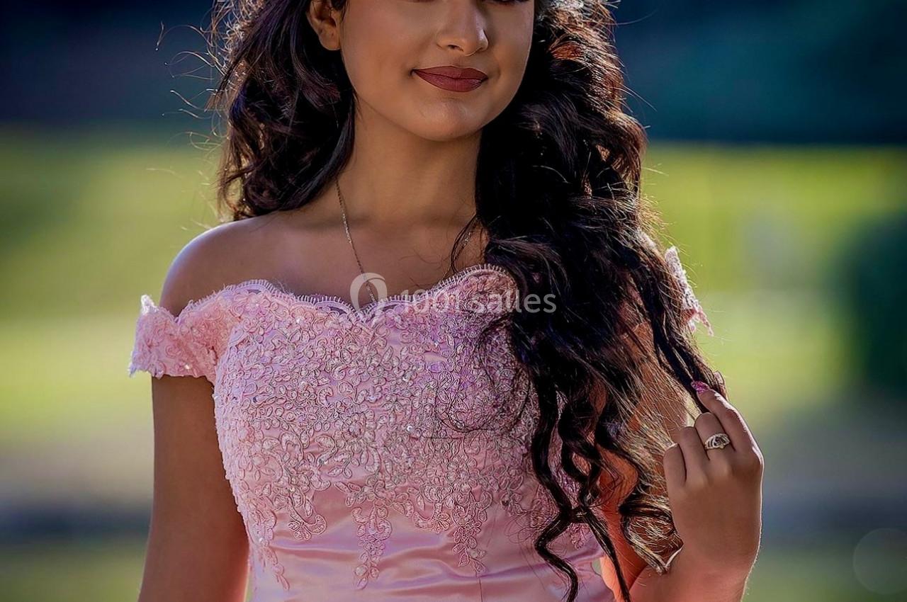 Jeune femme portant une robe rose élégante et une couronne, posant en extérieur avec un fond flou de verdure.