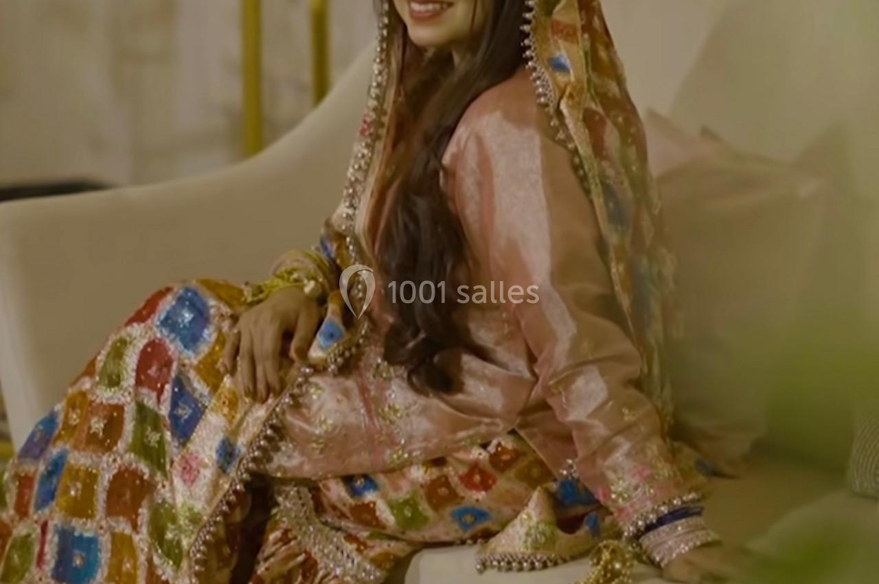 Femme souriante en tenue traditionnelle colorée, assise sur un canapé dans un décor intérieur élégant.