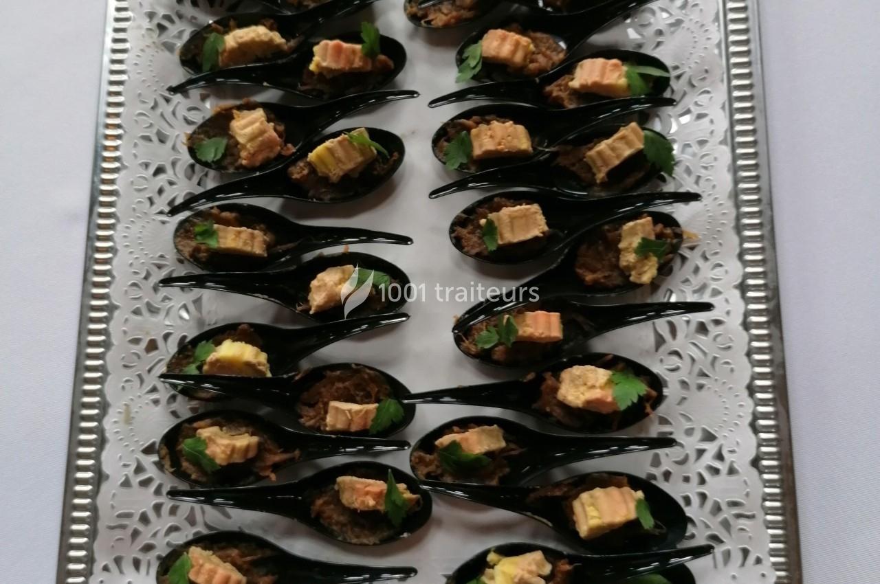 Cuillères apéritives noires garnies de morceaux de foie gras, herbes fraîches et accompagnements, présentées sur un plateau…