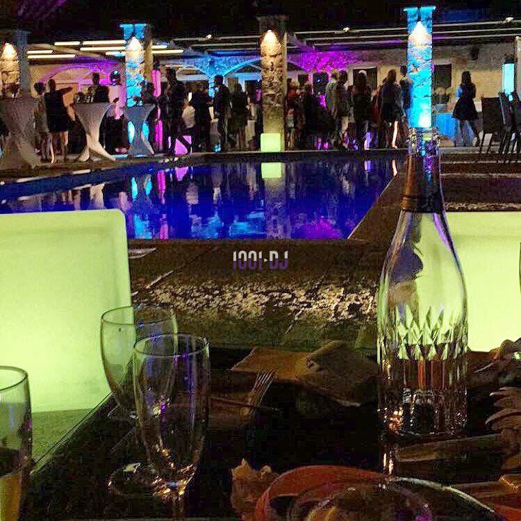 Vue d'une soirée en extérieur près d'une piscine éclairée, avec des tables dressées et des invités en arrière-plan.