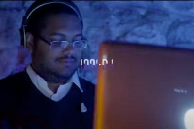 Un homme portant des écouteurs travaille sur un ordinateur portable dans un environnement faiblement éclairé.