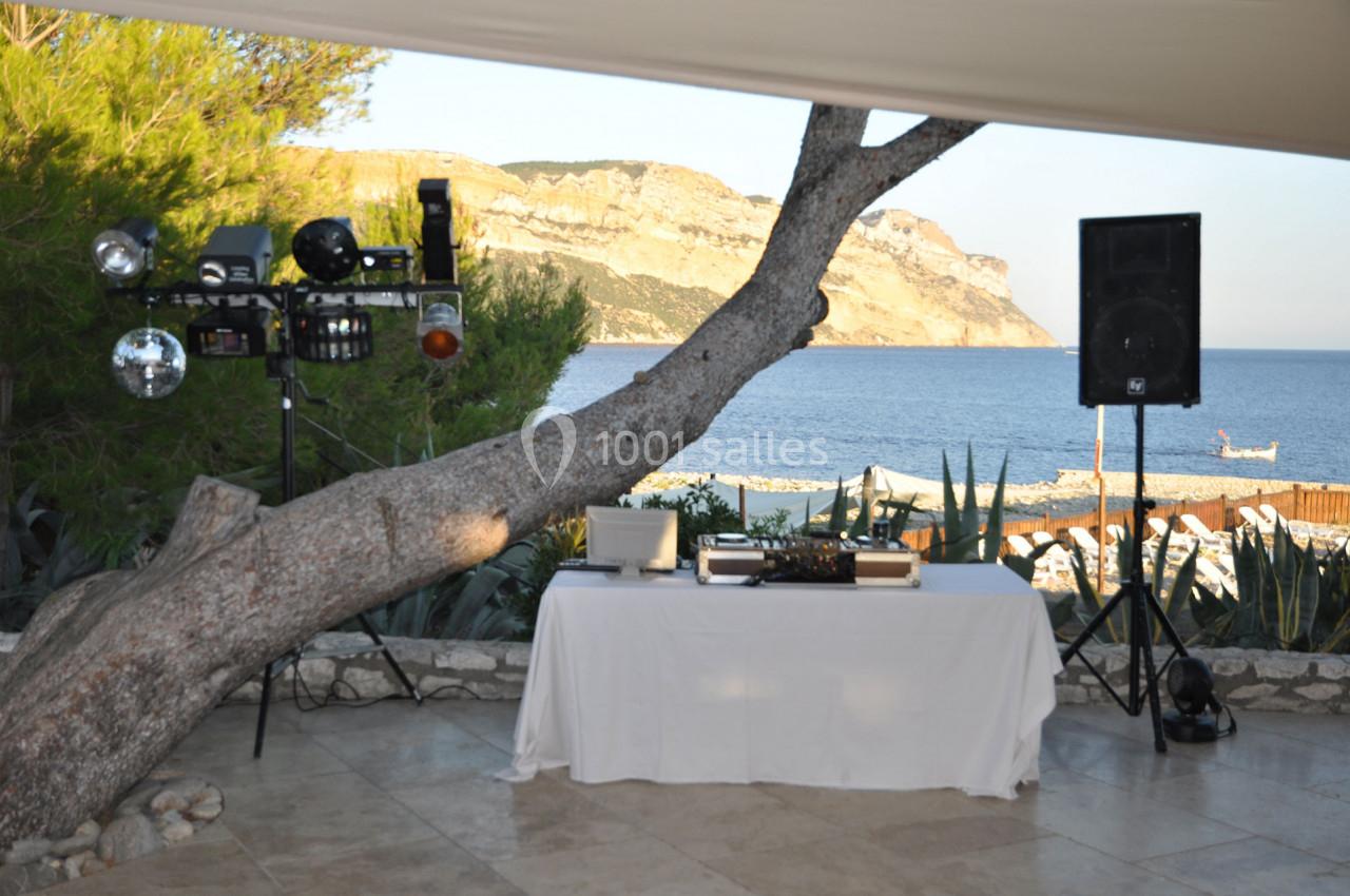 Table de mixage sous un auvent avec vue sur la mer, un arbre incliné et des équipements audio-visuels à proximité.