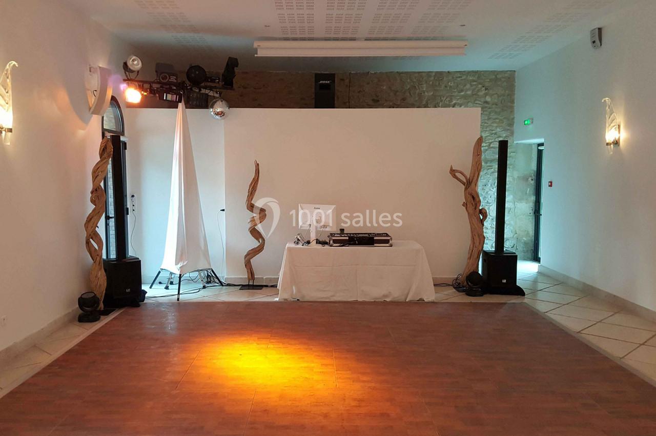 Salle vide avec parquet, éclairage tamisé, table de DJ équipée et décorations en bois torsadé.
