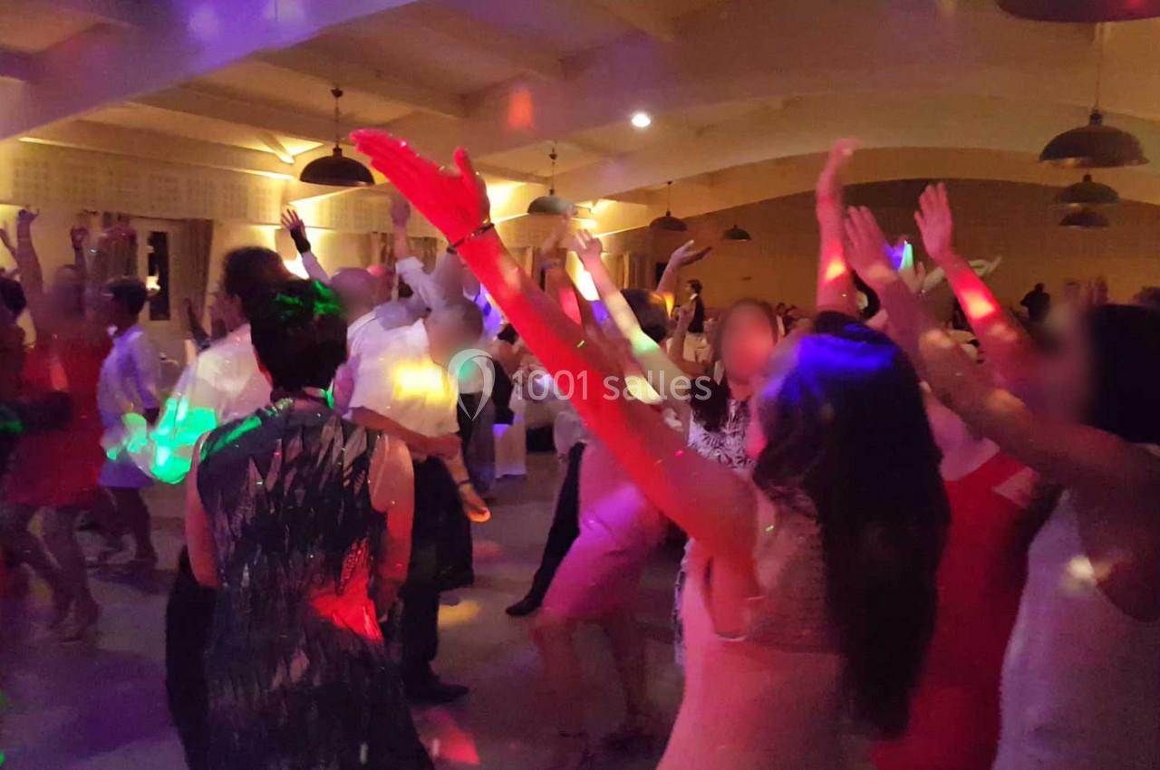 Des personnes dansent sous des lumières colorées dans une salle éclairée, bras levés et ambiance festive.