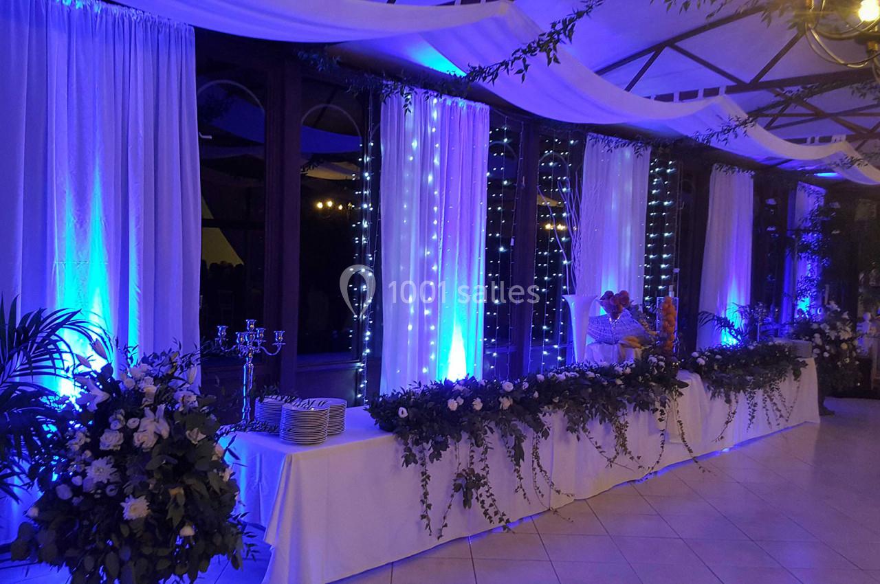 Salle de réception décorée avec des guirlandes lumineuses, des rideaux blancs et des arrangements floraux.