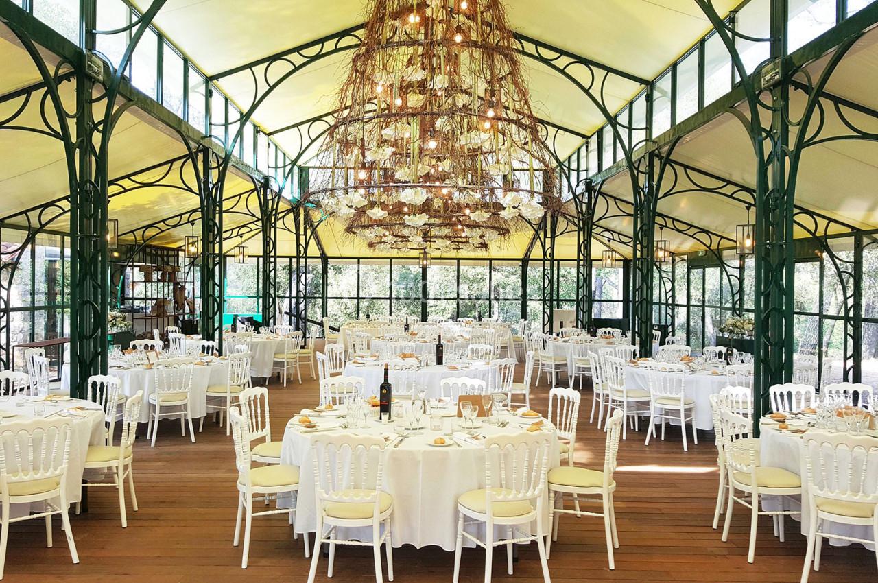 Salle de réception lumineuse avec tables rondes dressées, chaises blanches et grande suspension centrale en branches.