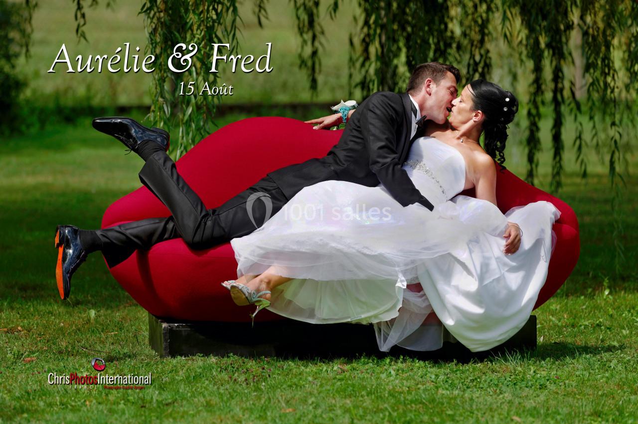 Un couple en tenue de mariage s'embrasse allongé sur un canapé rouge dans un jardin verdoyant.