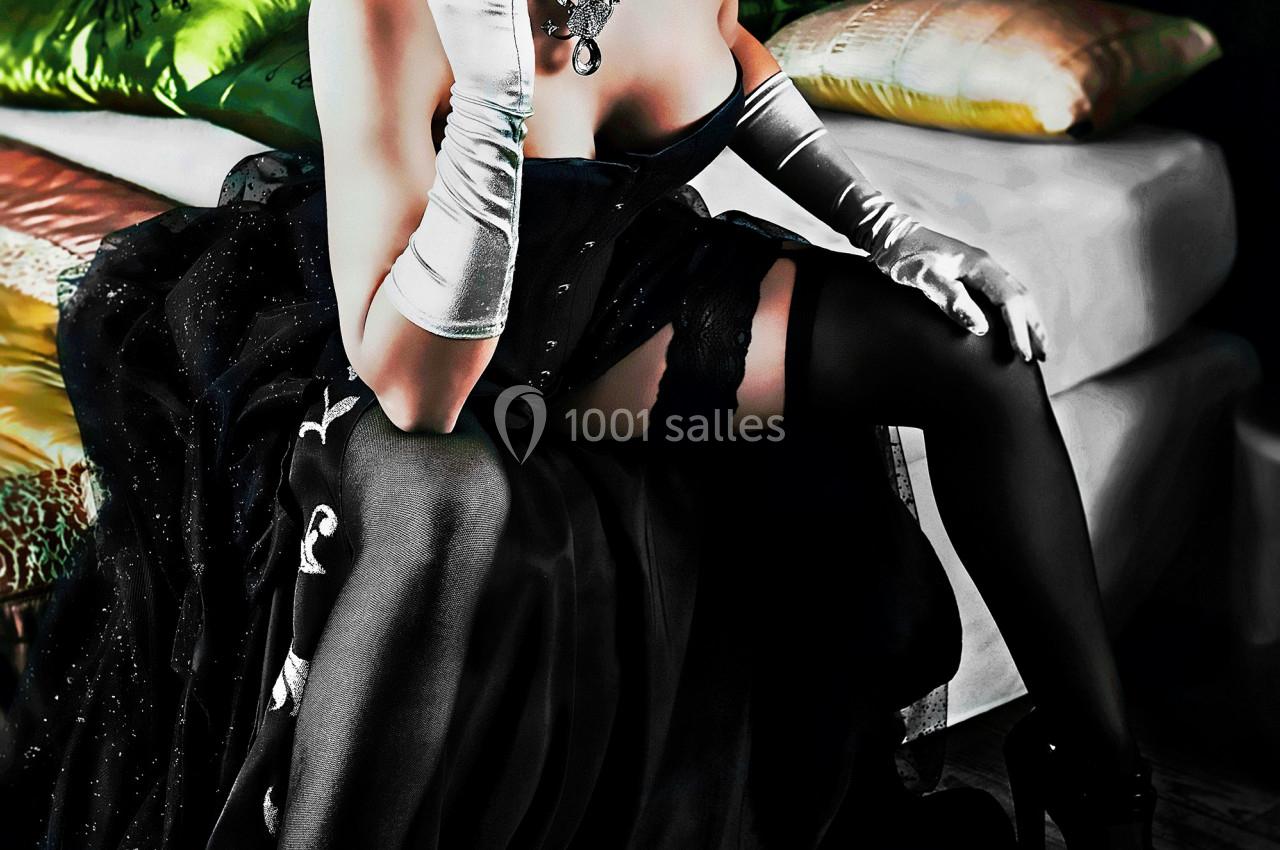 Femme en tenue élégante rétro, portant un corset noir, des gants blancs et un voile, assise sur un lit.