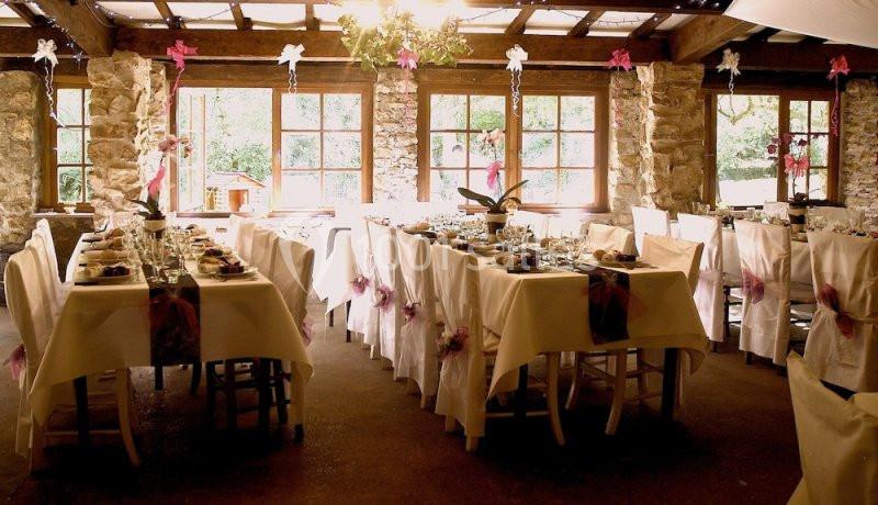 Salle de réception lumineuse avec des tables décorées de nappes blanches, rubans roses et vaisselle élégante.