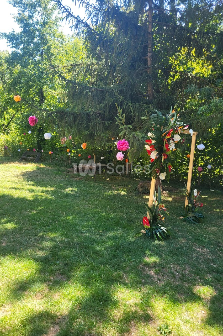 Décoration florale colorée suspendue dans un jardin verdoyant avec un cadre en bois orné de fleurs tropicales.