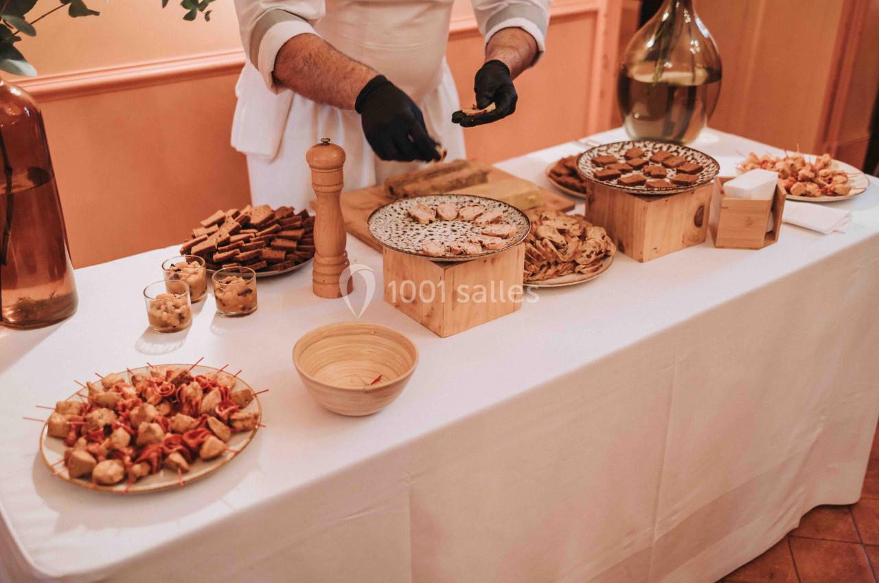 Un chef prépare un buffet composé de biscuits, toasts et amuse-bouches sur une table blanche.