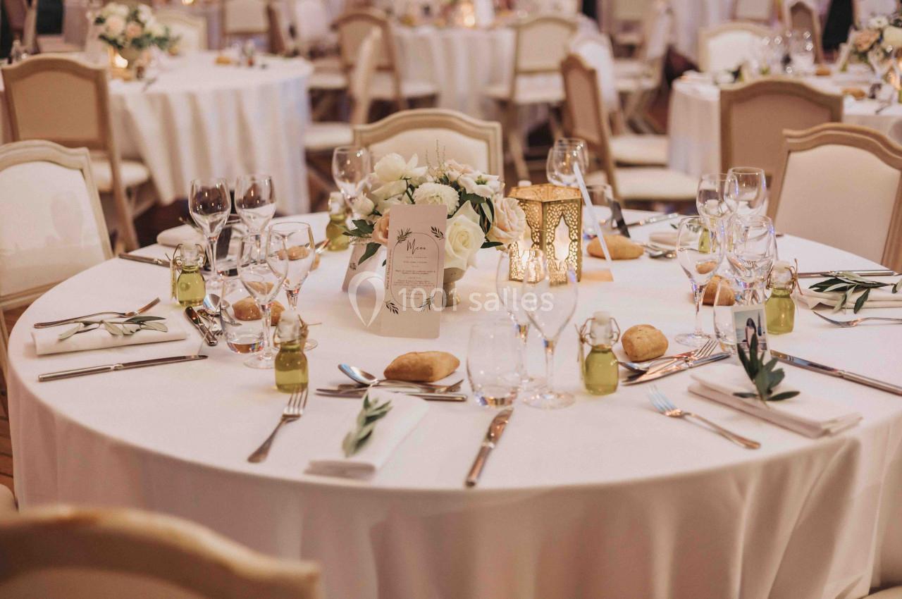 Table élégamment dressée avec nappes blanches, vaisselle raffinée, bougie décorative et centre de table floral.