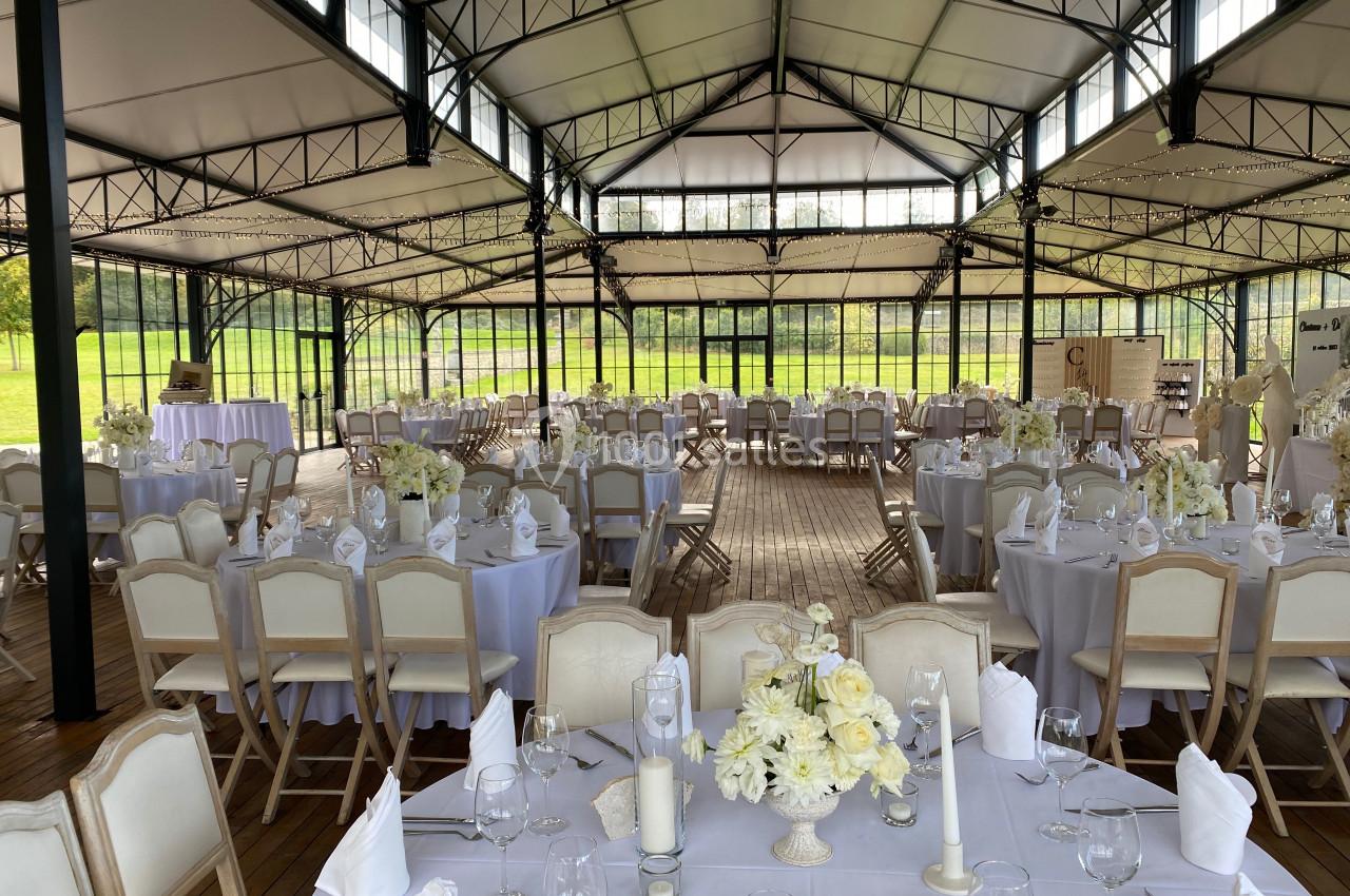 Salle de réception lumineuse avec tables rondes décorées de nappes blanches et de bouquets de fleurs claires.