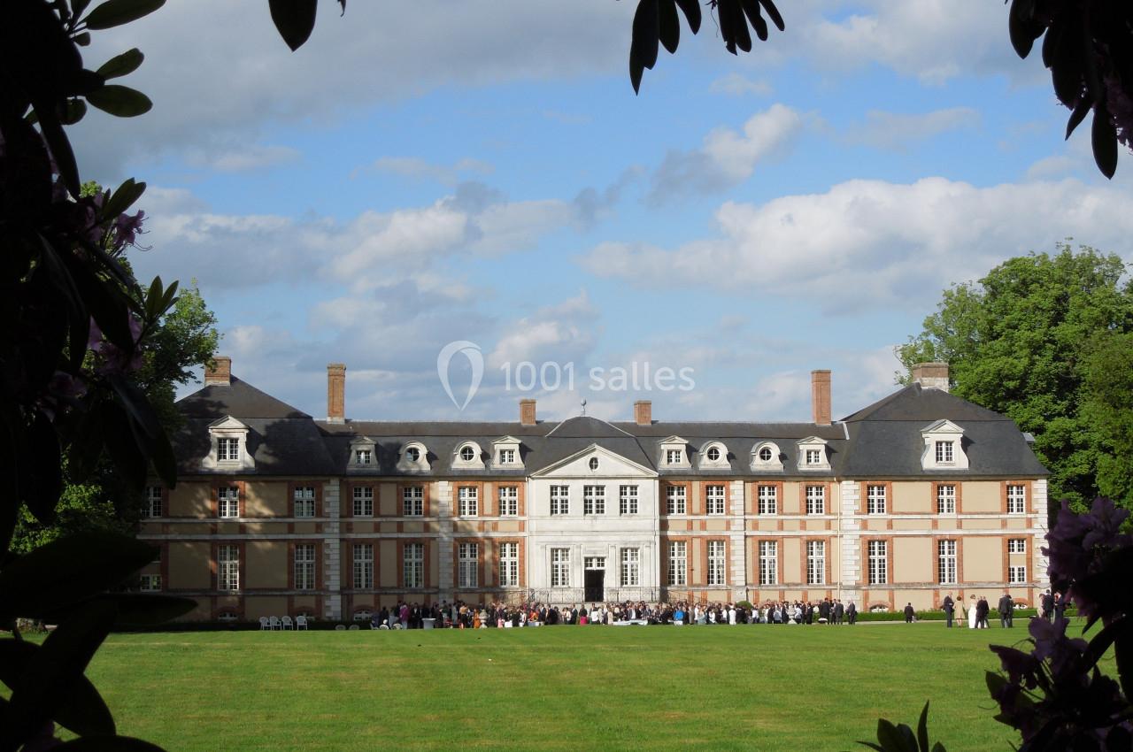 Façade d'un château en briques et pierre entouré de verdure, avec des visiteurs rassemblés sur la pelouse.