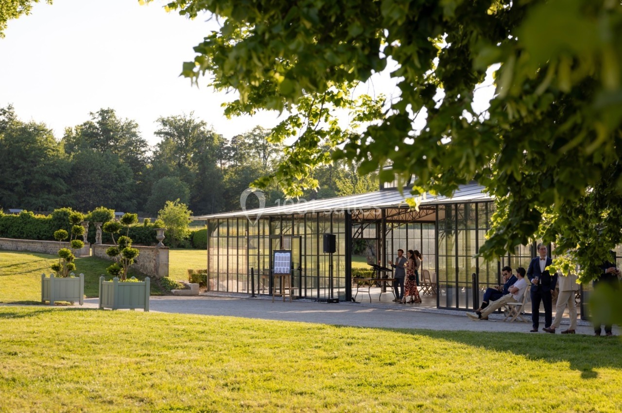 Serre vitrée entourée de verdure, avec des personnes à l'intérieur et à l'extérieur dans un cadre champêtre.