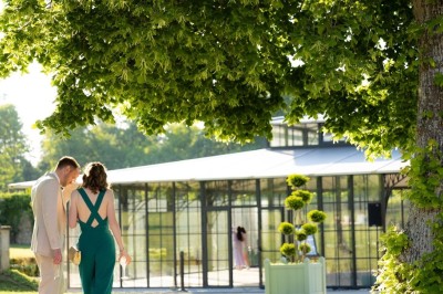 Façade d'un château en pierre et briques entouré d'une pelouse et d'arbres sous un ciel bleu clair.