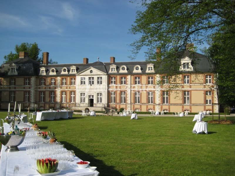 Façade d'un château entouré d'un grand jardin, avec des tables dressées pour un événement en plein air.