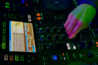 Miniature DJ La Queue-les-Yvelines (Yvelines) - DJ Braz #24 Main ajustant les réglages sur une table de mixage DJ illuminée par des lumières colorées.