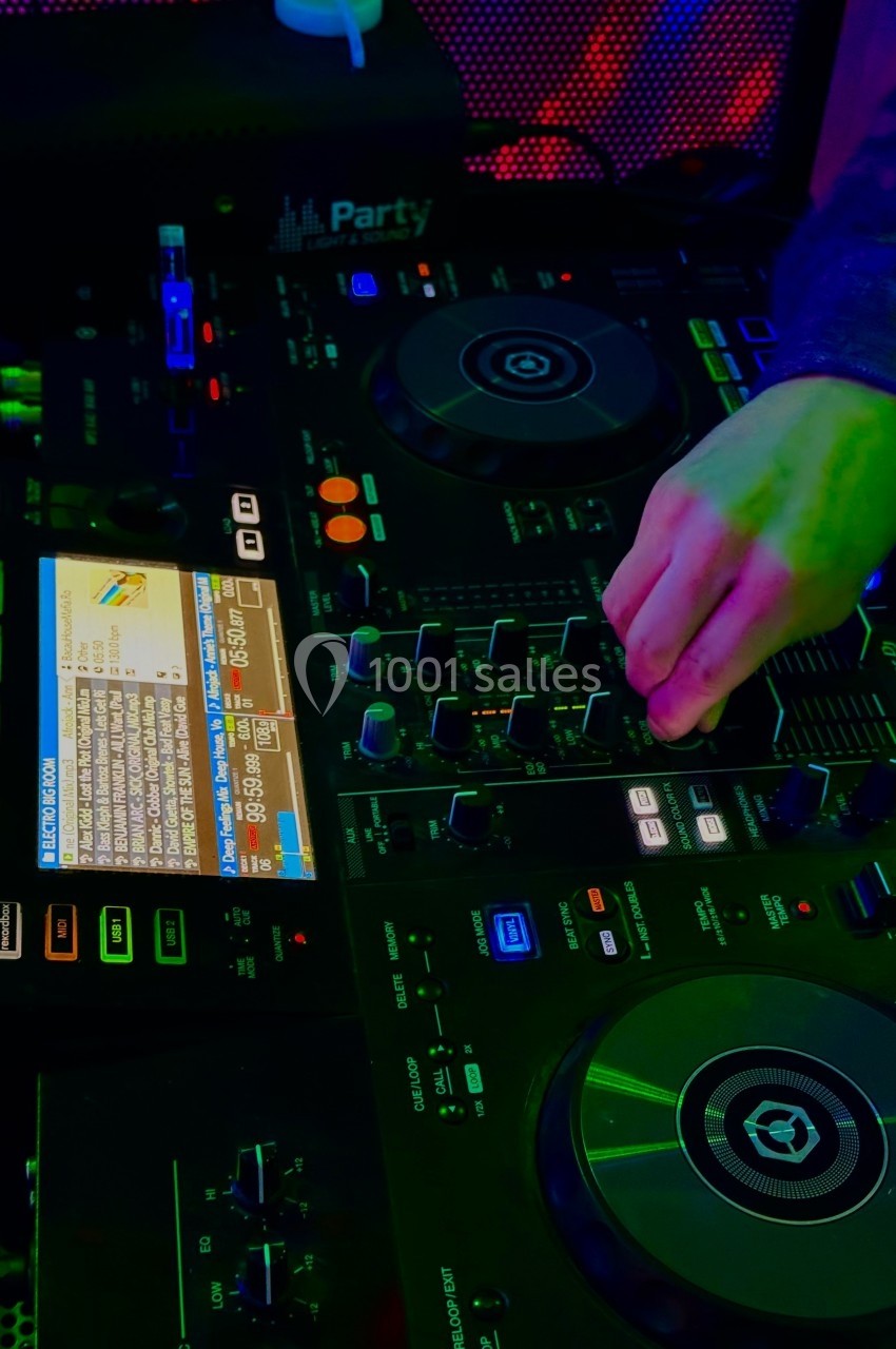 Main ajustant les réglages sur une table de mixage DJ illuminée par des lumières colorées.