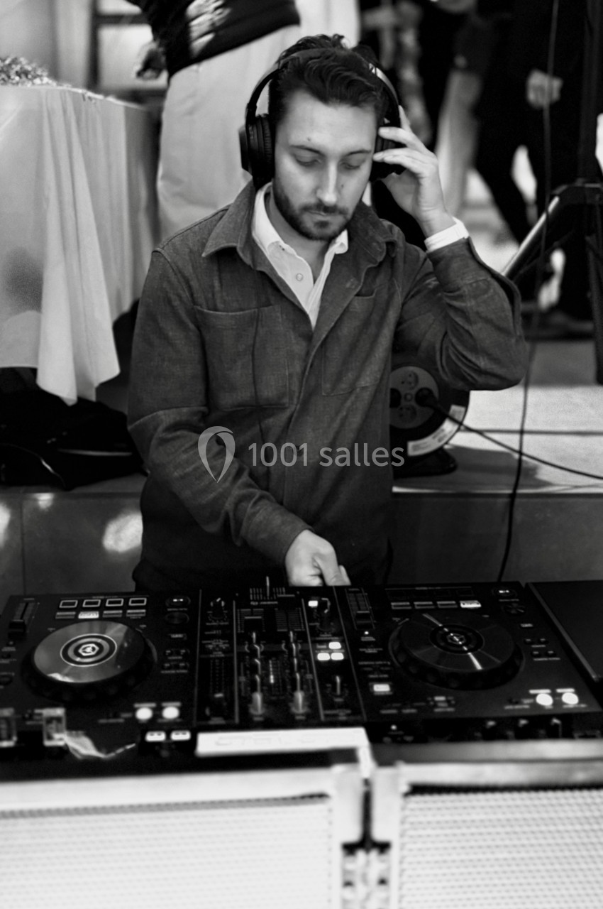 Un DJ mixant de la musique sur une table de mixage, portant un casque audio dans un environnement intérieur.